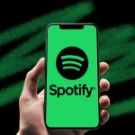 Hand holding a mobile phone with the Spotify app opened.